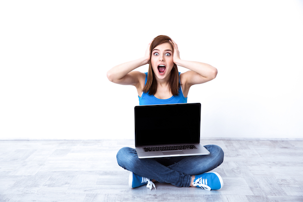 Surprised young woman sitting at the floor with laptop